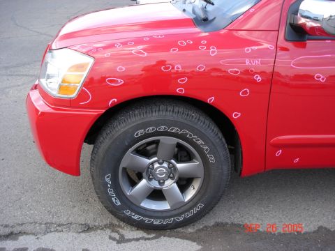2005 Nissan Titan - Front fender of a red 2005 Nissan Titan with hail damage circled. The word 'RUN' is written on the door.
