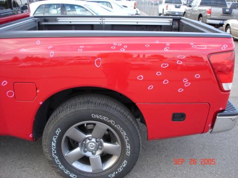 2005 Nissan Titan - This 2005 Nissan Titan shows significant hail damage on its red truck bed, with numerous circular marks circled in white.