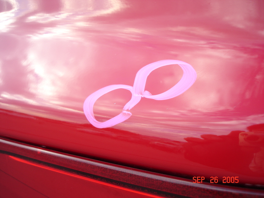 Two hail dents circled in white grease pencil on glossy red truck body panel