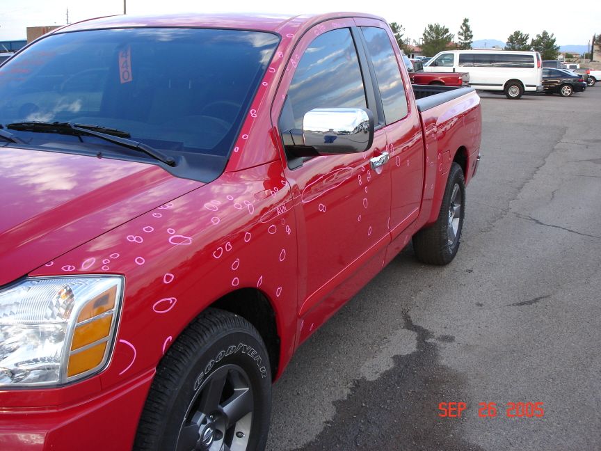 Red Nissan pickup with hail dents circled in white grease pencil on hood and doors