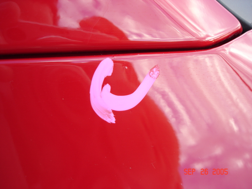 Hail dent circled in white grease pencil on red pickup body panel near hood gap