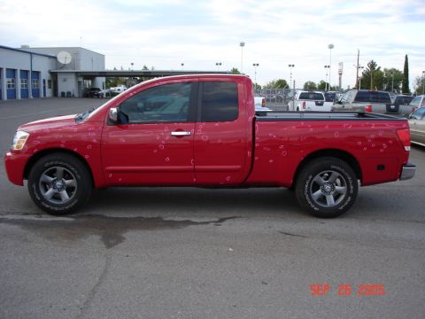 2005 Nissan Titan - Red pickup truck shows extensive hail damage on its side panels.