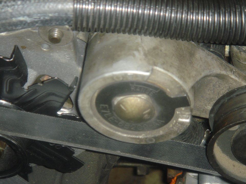 Close-up of an engine belt tensioner with part number E7LE-6B209-AA visible