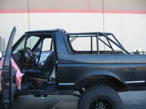 1992 Ford Bronco - Driver-side view of a black full-size Ford Bronco with its rear top removed and a custom tubular roll cage fabricated over the open rear se…