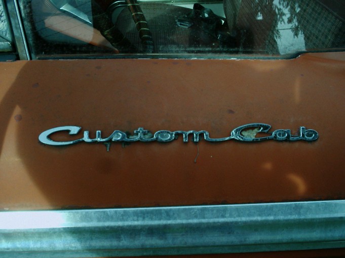 Chrome 'Custom Cab' script emblem on faded orange truck door panel