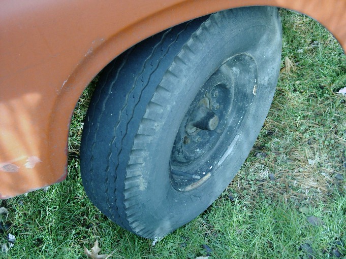 Bias-ply tire on plain steel wheel under orange truck fender, on grass