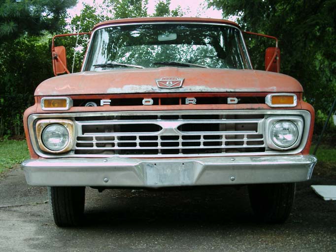 Front of faded orange Ford truck, FORD grille lettering, round headlights, on driveway