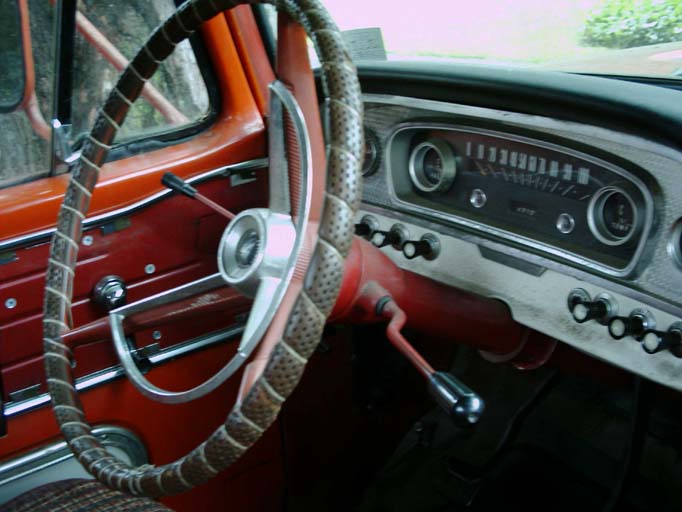 Red column shifter pulled down in vintage Ford pickup cab, laced wheel and painted dash