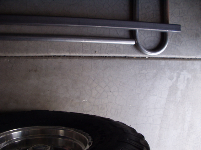 Bare metal tubular bumper bar on concrete floor next to a chrome wheel and tire