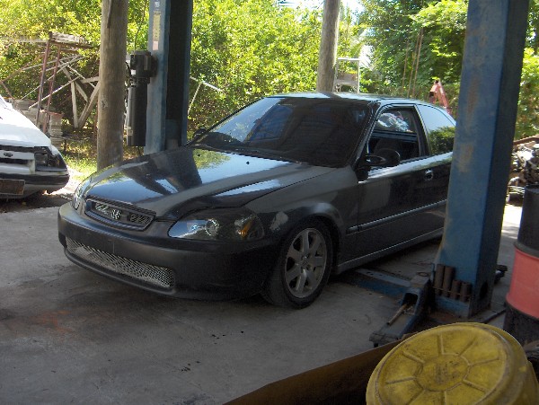 Dark gray Honda Civic hatchback parked in workshop near blue two-post lift
