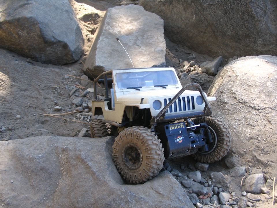 Tan Jeep-bodied RC crawler perched on rock, antenna up, chunky off-road tires