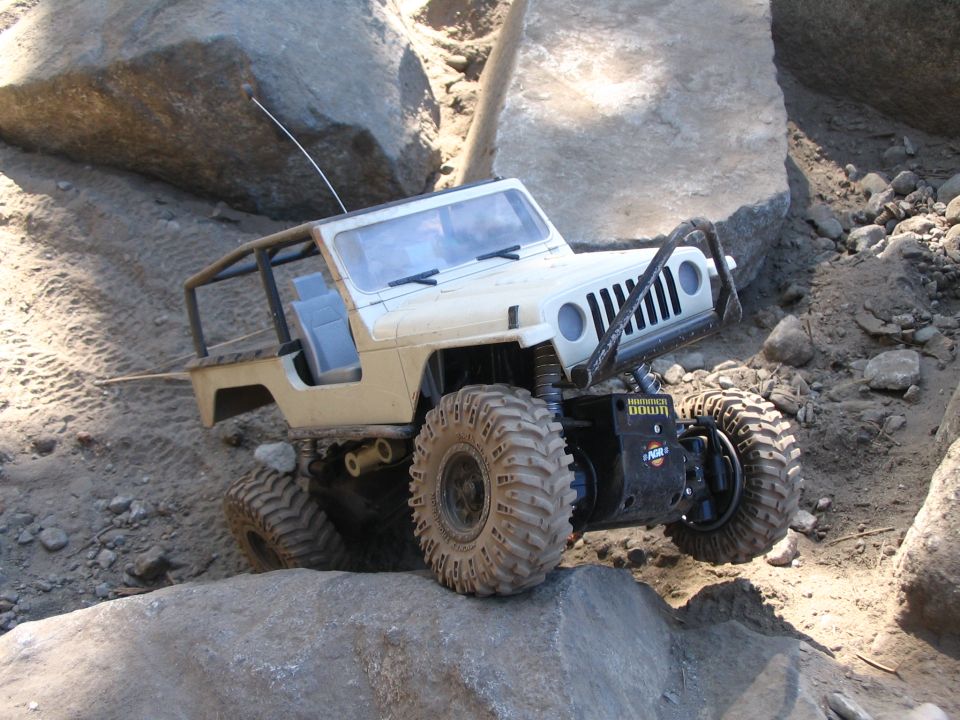 RC rock crawler tilted on boulders, suspension flexed, blue motor exposed