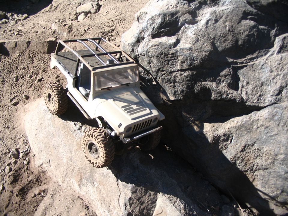 Topless tan RC crawler with roof rack hood-down on a rock shelf, overhead view