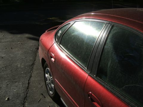 1998 Ford Taurus - Side view of a red 1998 Ford Taurus sedan with sun glare on the windows.