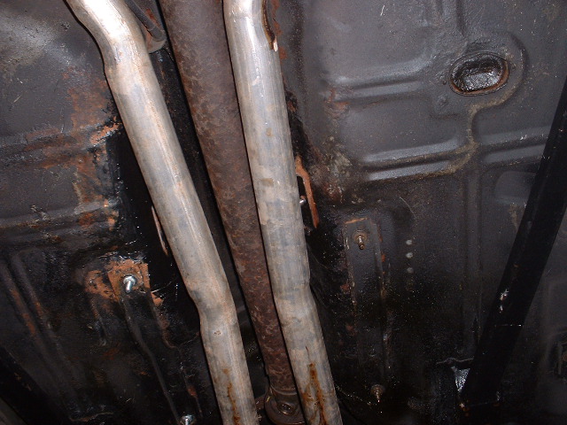 Underside of car showing dual exhaust pipes, driveshaft and surface-rusted floor pan
