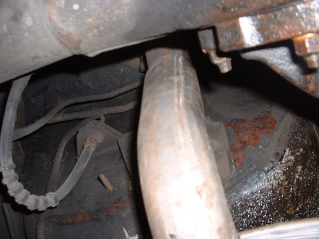 Close-up of a rusty exhaust pipe and brake line under a vehicle