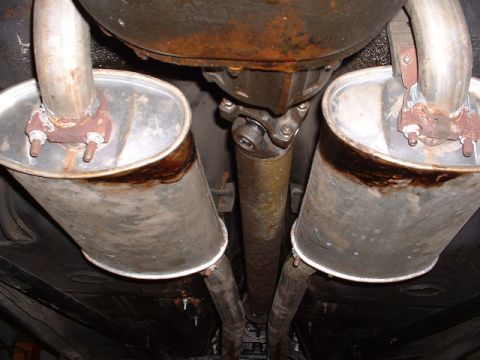 1978 Ford Mustang II - Underside view of a vehicle's rusty dual exhaust system, showing mufflers and driveshaft, with visible water stains.