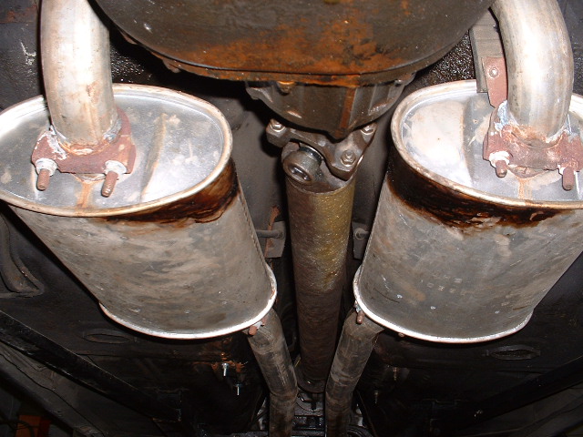 Underside view of a rusty dual exhaust system with mufflers and driveshaft