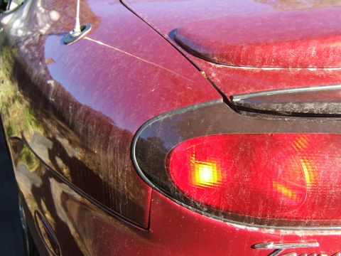 1998 Ford Taurus - Close-up of a dusty red car's rear quarter panel and illuminated taillight, showing the texture of the dirt.