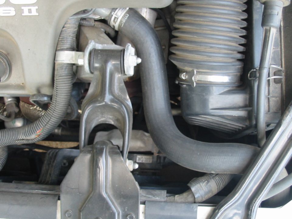 Engine bay close-up with black mount bracket, gray coolant hose, and ribbed air intake boot.
