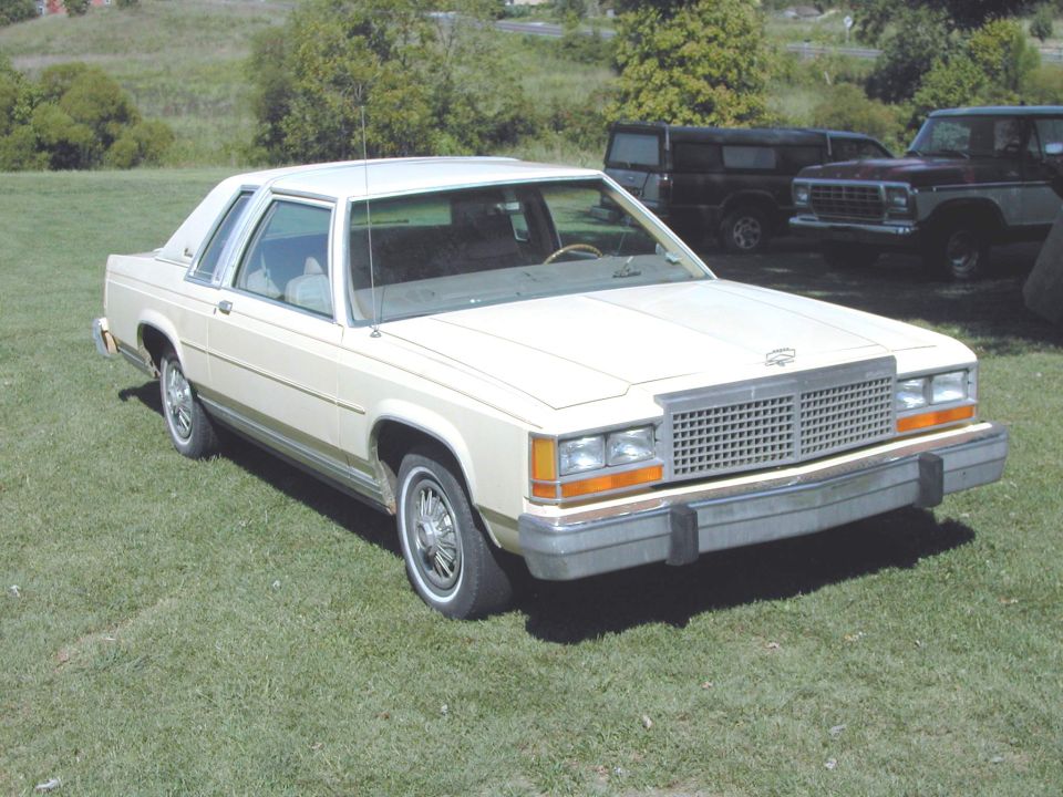 1985 Ford Crown Victoria LTD parked on grass, front grille and headlights visible. Two other vehicles in background