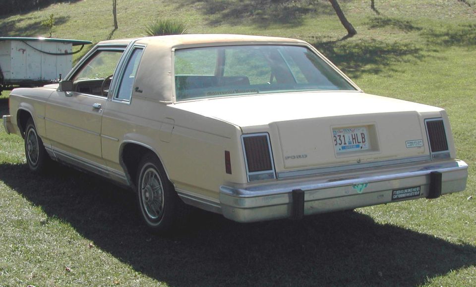 Tan Ford Crown Victoria parked on grass, rear view. License plate 331 HLB