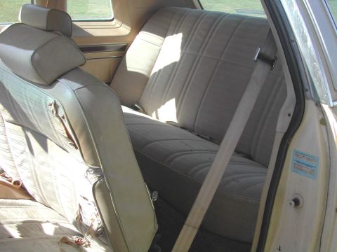 1985 Ford LTD Crown Victoria - Interior view of a car with beige fabric seats and visible seatbelts. A sticker is present on the door jamb.