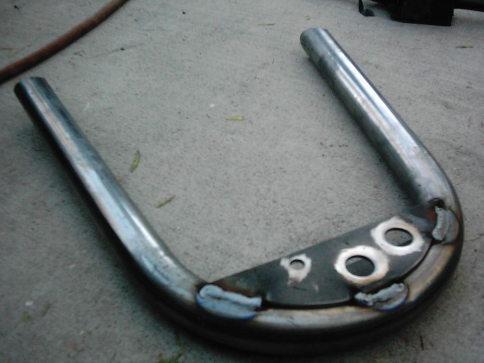 U-shaped metal tube with a flat mounting plate two large holes and two smaller holes, welded together and resting on concrete