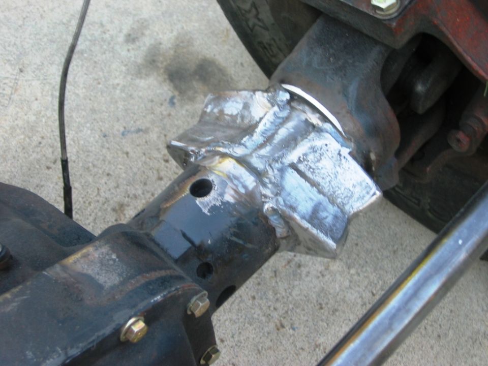 Close-up of a fresh weld joining a metal bracket to a black axle/suspension component.