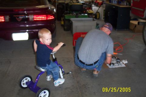 1995 Ford F-350 - A young child rides a tricycle in a garage while an adult works on vehicle components on the floor.