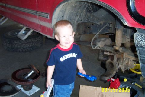 1995 Ford F-350 - A young child stands in a garage next to a vehicle undergoing repairs, holding toy tools.