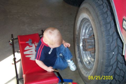 1995 Ford F-350 - A toddler sits on a red creeper beside a large tire in a garage.