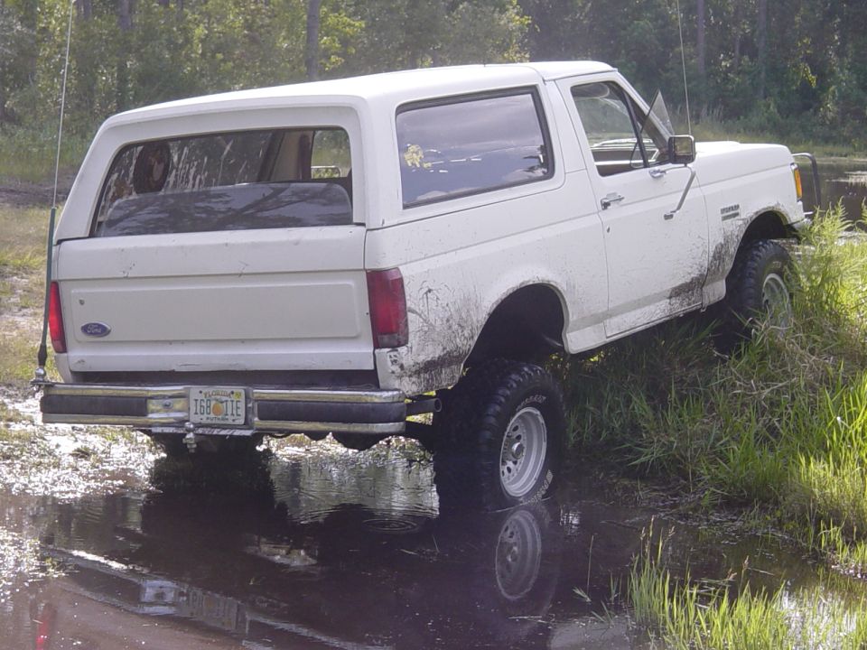 White 1989 Ford Bronco driving through mud and water