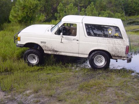 1989 Ford Bronco - This 1989 Ford Bronco navigates through a wet, grassy terrain with mud splattered on its body.