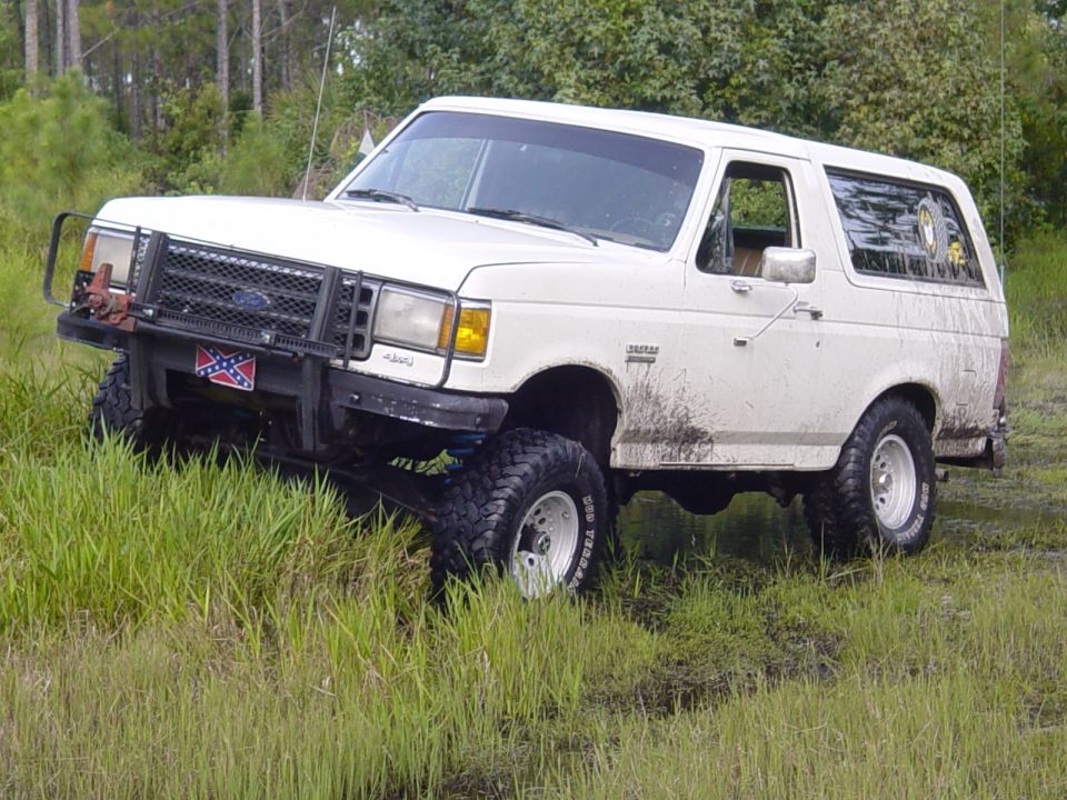 White Ford Bronco with brush guard and lifted suspension driving through tall grass