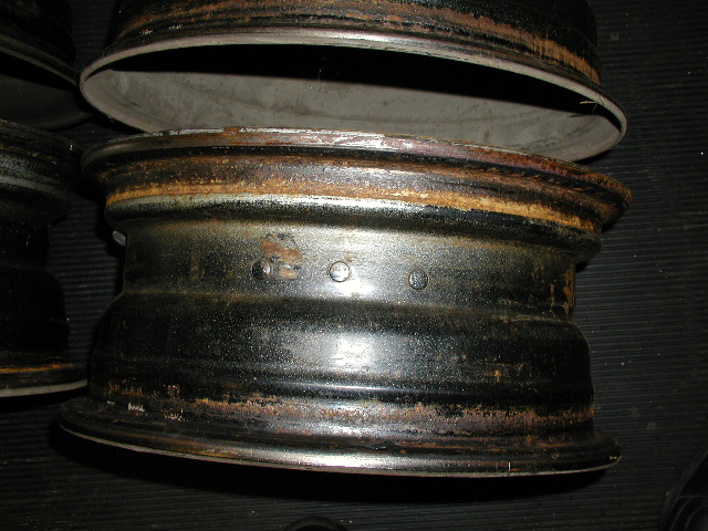 Stripped bare steel wheel rims with surface rust stacked on a dark shop floor