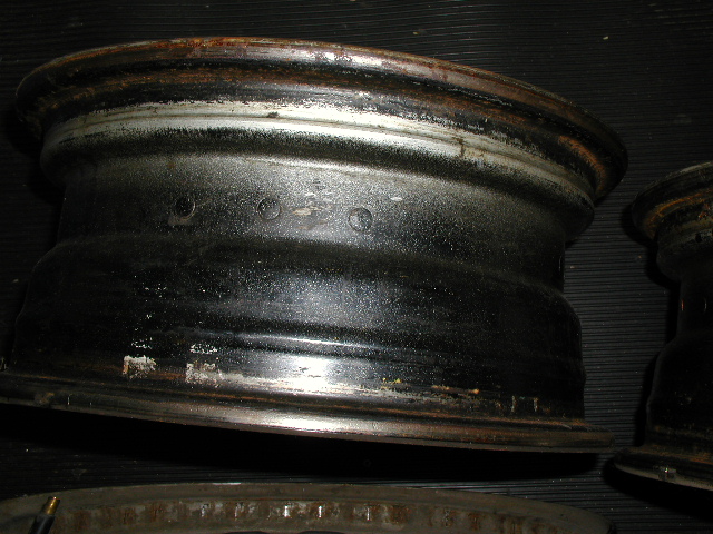 Bare rusty steel wheel rims on a dark ribbed surface