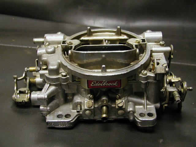 Edelbrock four-barrel carburetor on a workbench, front view with red nameplate