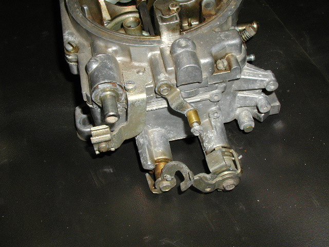 Close-up of a four-barrel carburetor's throttle linkage on a black workbench