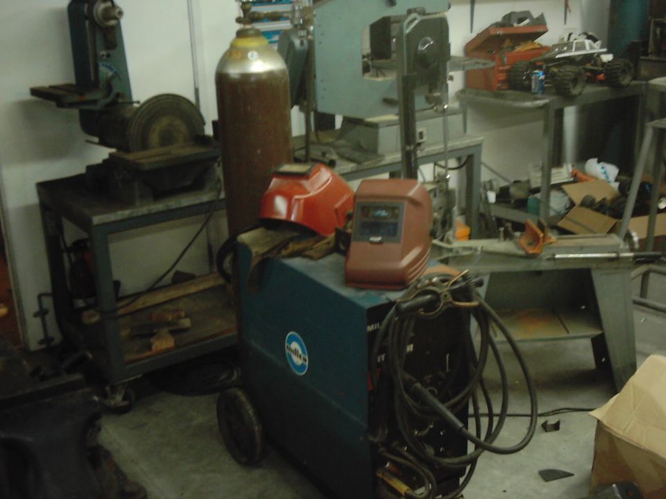 Miller welding machine with two welding helmets, gas cylinder, and various workshop tools