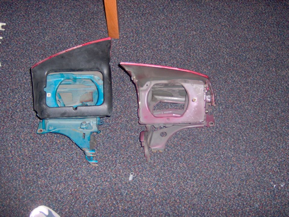 Two car headlight assemblies, one black and blue, one red and silver, on carpet