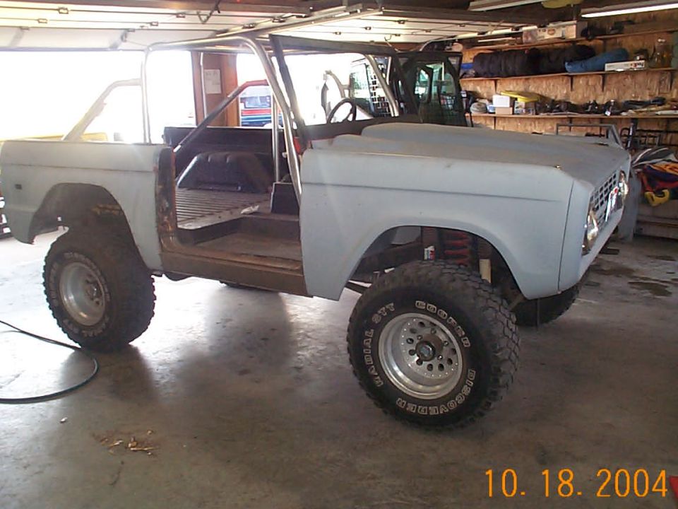 Lifted primer-gray Ford Bronco with no doors or top in a garage, large Cooper tires, dated 10.18.2004