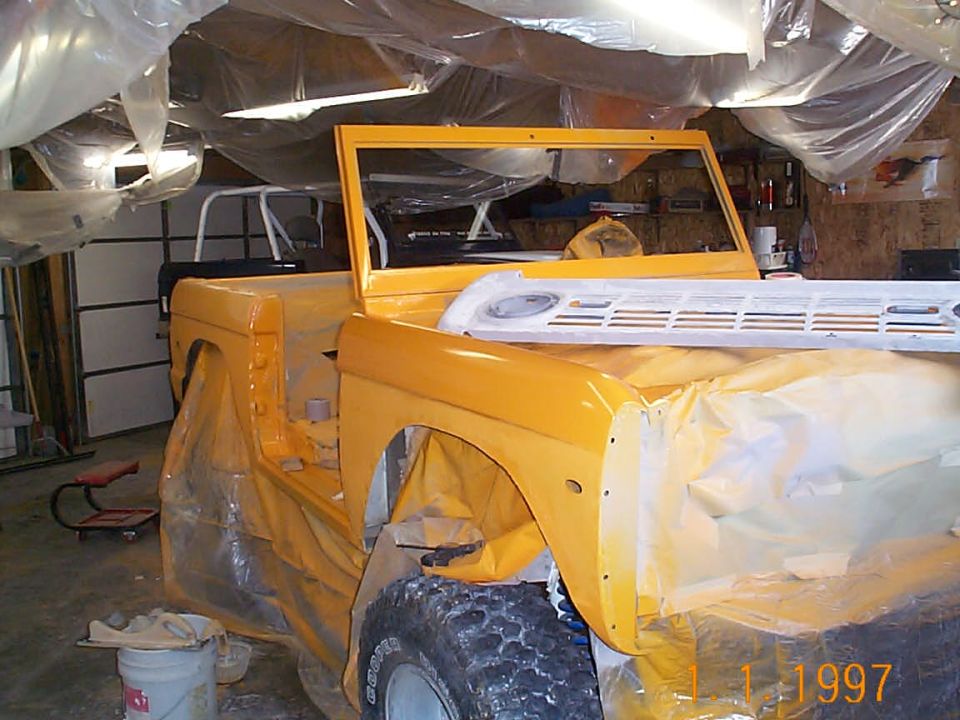 1974 Ford Bronco body, yellow primer, covered in plastic sheeting, in garage
