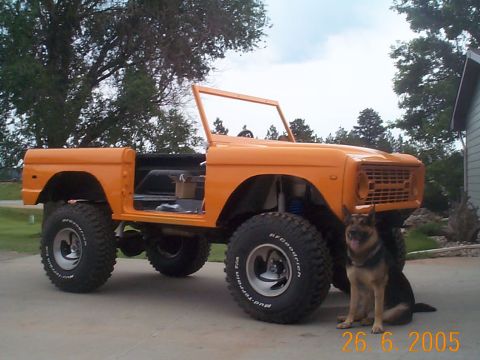 1974 Ford Bronco - A German Shepherd sits next to an orange Ford Bronco with its doors off, parked on a driveway.