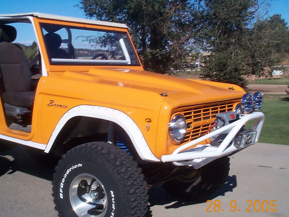 Orange 1974 Ford Bronco with white trim, off-road tires, and a winch on the front bumper