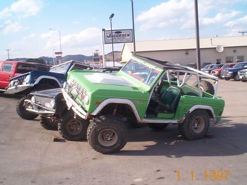 1977 Ford Bronco - Several SUVs are parked in a lot, with a green Ford Bronco in the foreground.