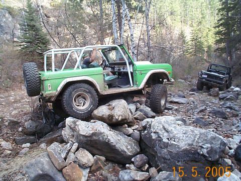 1977 Ford Bronco - Two SUVs navigate a rocky trail through a wooded area.