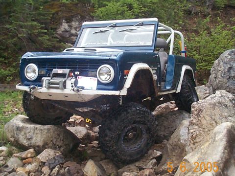 1977 Ford Bronco - This modified SUV is shown off-roading on a rocky trail, its large tires gripping the stones.
