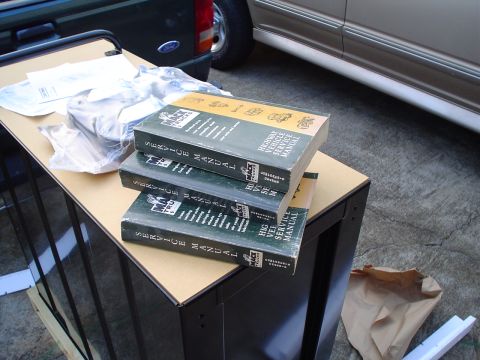 1966 International School Bus - Three Mack Trucks service manuals are stacked on a table, with parts and other vehicles visible in the background.