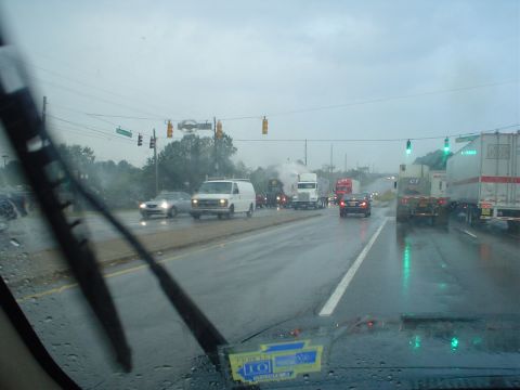 1966 International School Bus - A rainy day traffic scene with multiple vehicles on the road, viewed from inside a car.